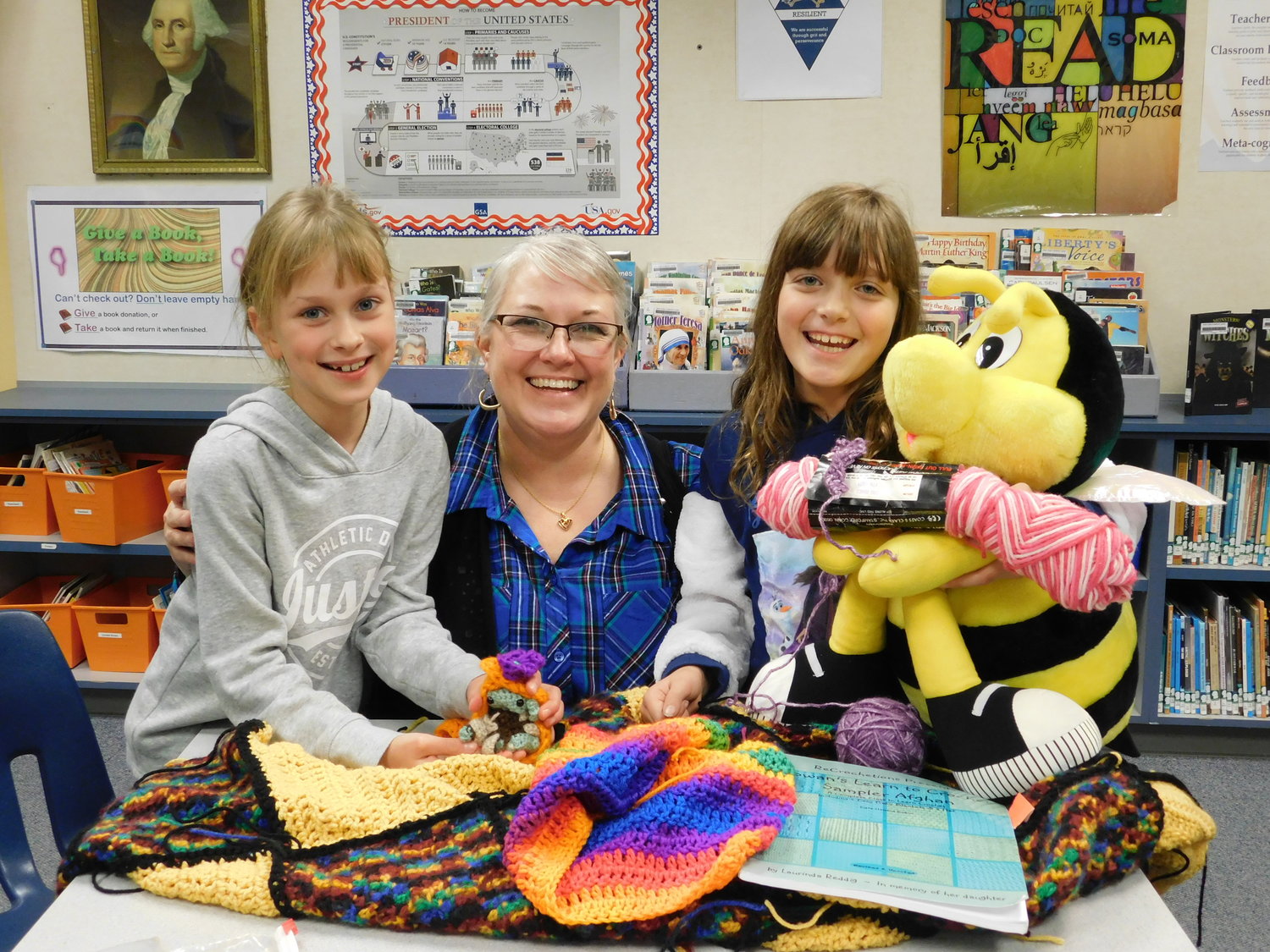 Third-graders Marta Krawczyk, left, and Liberty Glessing sit with South Ridge Elementary School librarian Emily Crawford to show their Crochet Club projects. 
