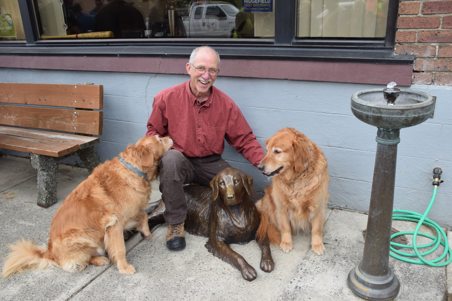 Former Ridgefield Mayor and community leader Tevis Laspa crowds around a bronze Golden Retriever statue in front of city hall along with his dogs Zoe, left, and Daisy, right, during an official unveiling of the statue, donated to the city by Laspa, May 4.