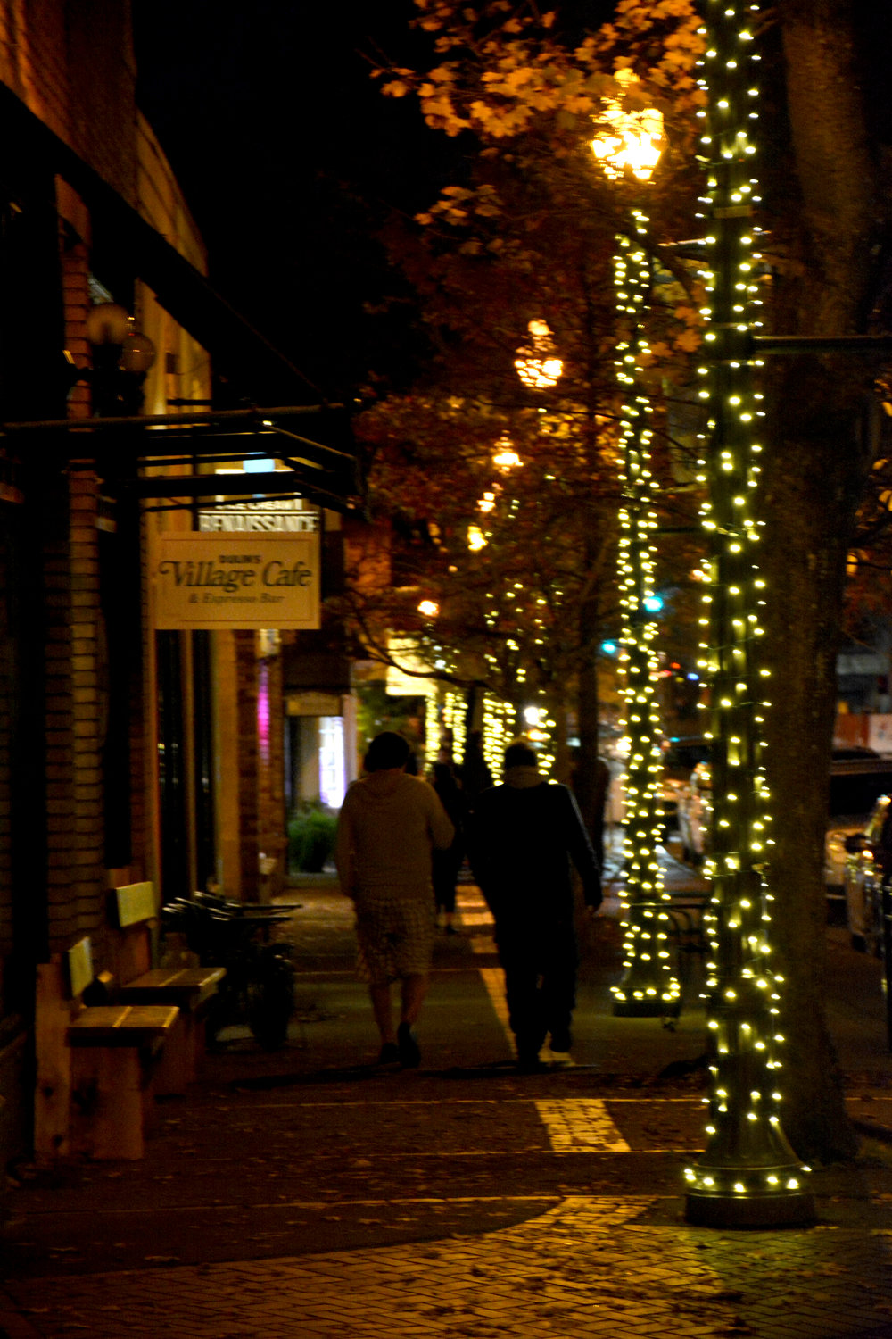 People walk down the sidewalk of Main Street in the Uptown Village, illuminated by recently strung Christmas lights. The Uptown Village Association raised close to $7,000 to pay for the lights and installation, part of their efforts to celebrate the holidays.