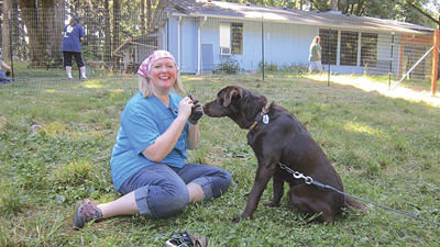 FENCES FOR FIDO volunteer Andrea Armstrong gives a homemade doggy treat to DJ, the chocolate lab, during DJ’s Fences for Fido fence-build in 2014.