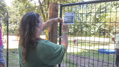 TRACY TRUSSLER, of Ridgefield, installs the Fences for Fido sign on her backyard fence. The volunteer-run Fences for Fido group built the fence for Trussler’s dog, DJ, in June of 2014. DJ is one of more than a 1,000 formerly chained-up pups that now roams free thanks to the efforts of Fences for Fido.