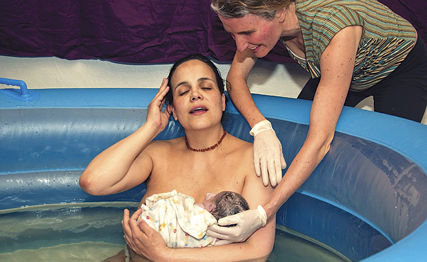 BATTLE GROUND MIDWIFE and naturopathic doctor Alexandra Demetro cradles the head of just-born baby Ina, while Ina’s mom, Rebecca, relaxes in her waterbirth pool.