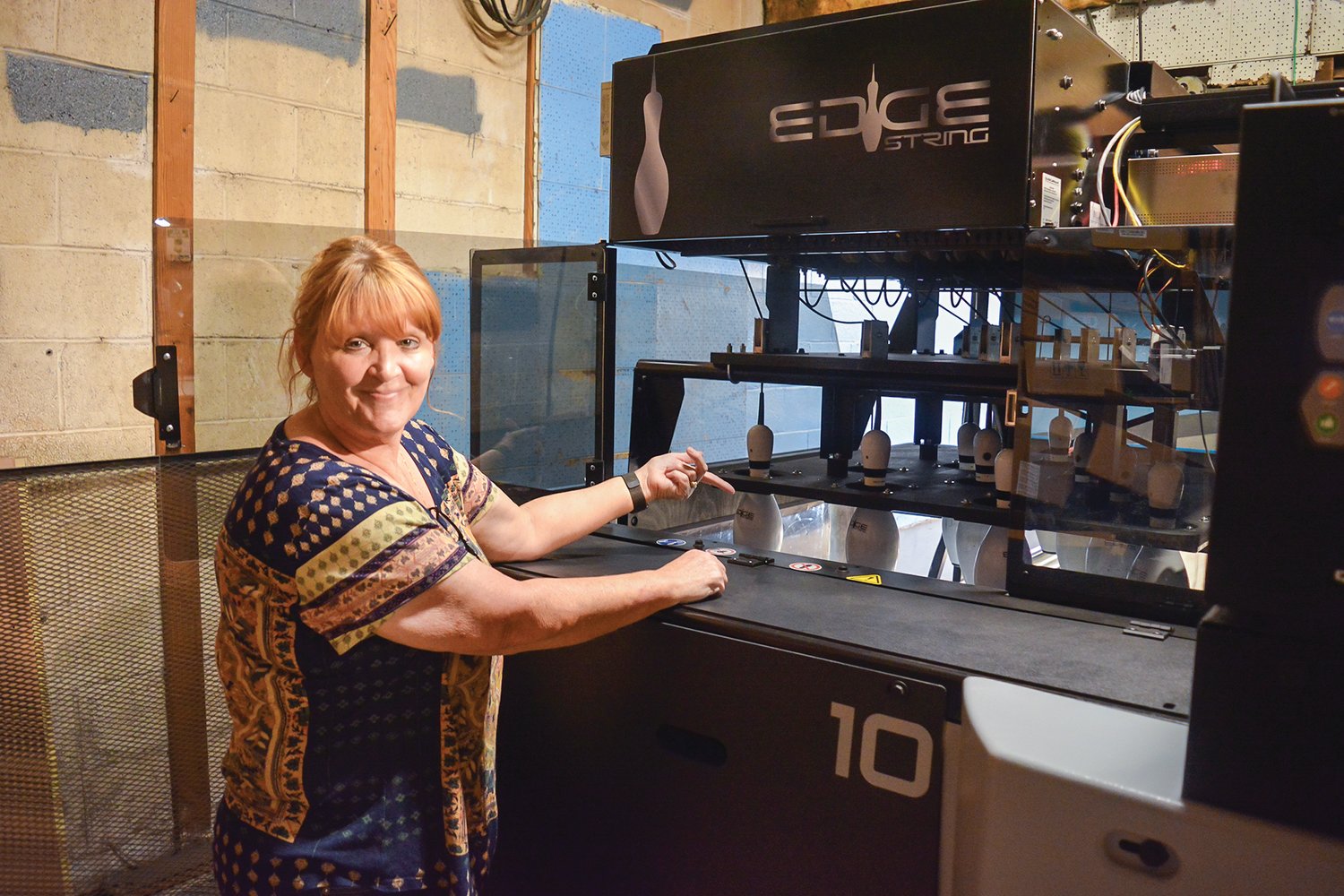 Tiger Bowl co-owner Robin Bailey shows off the Edge String Pinspotter at the alley in Battle Ground. The new pin-catching technology helps the business reduce its costs.
