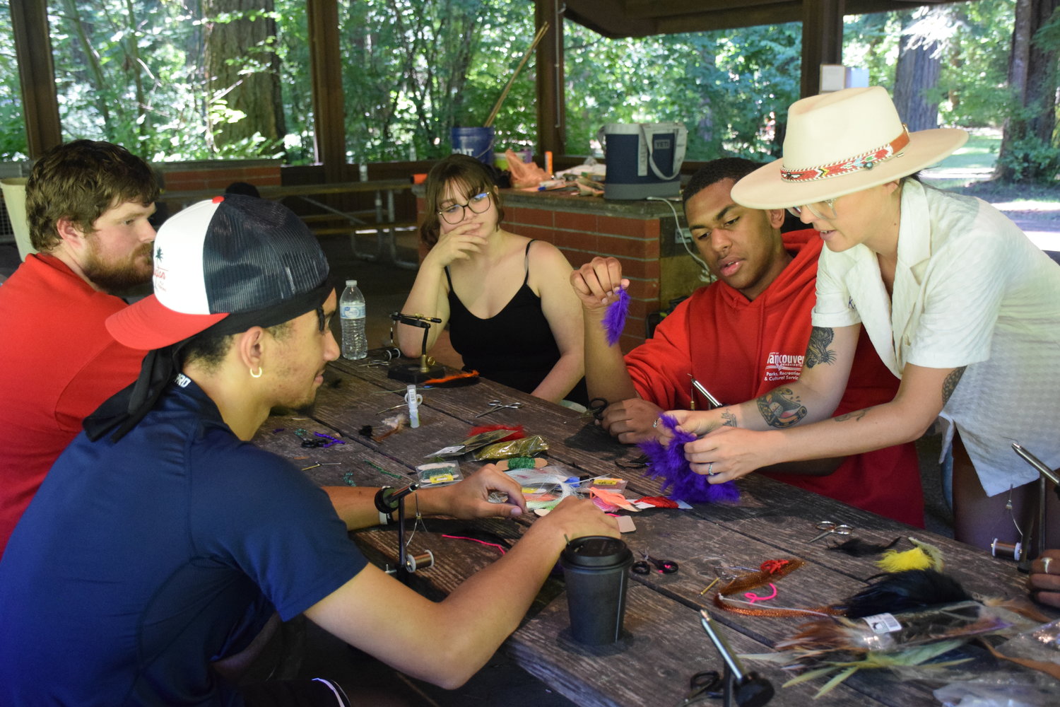 Kayla Lockhart, who is sporting a hat, teaches participants how to make a fishing fly at Battle Ground Lake State Park on July 20.