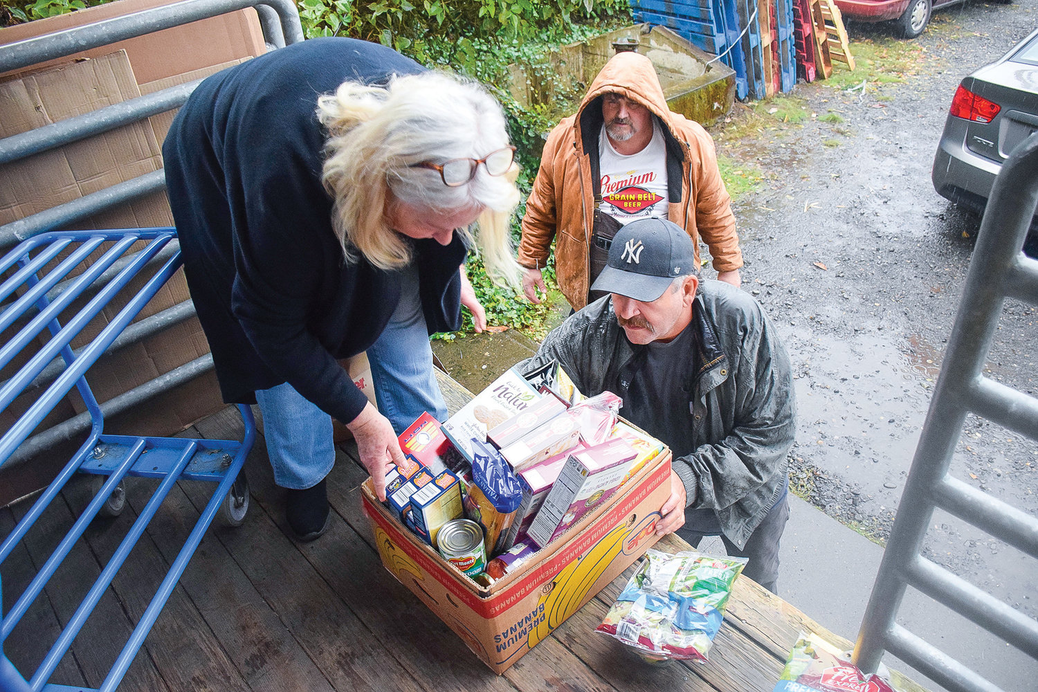 Neighbors Helping Neighbors food bank coordinator Pam Bong, left, hands a food box to volunteers Kevin Jochim, bottom, and Jeff Johnson so it can be placed in a vehicle at the food bank on Nov. 22.